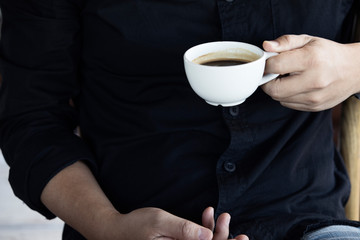 Hands of a man with a white cup of coffee in the morning, black shirt background,Close up 