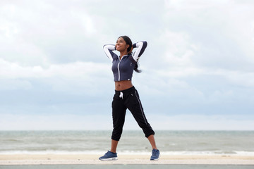 healthy african american woman relaxing with hands behind head at beach
