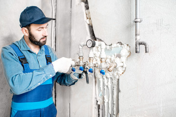 Workman in blue uniform installing water heating system on the construction site of a new house