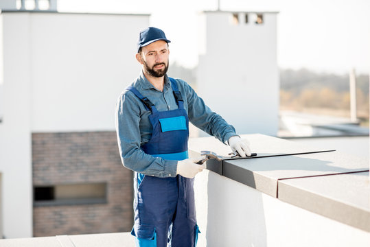 Builder in uniform mounting metal cover on the parapet of a new building