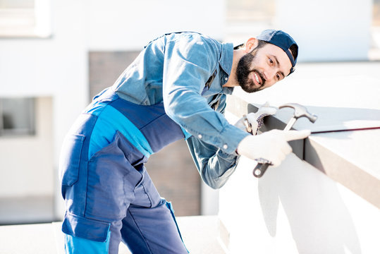 Builder in uniform mounting metal cover on the parapet of a new building