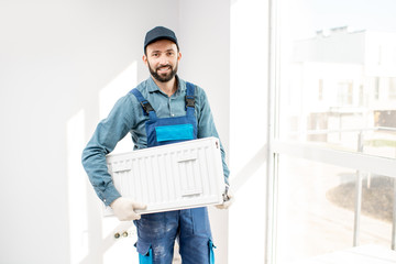 Portrait of a workman holding heating radiator in the white room
