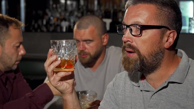 Bearded mature man smiling to the camera after tasting delicious whiskey. Group of mature men enjoying luxury alcohol drinks at the bar. Man tasting whiskey at the restaurant.