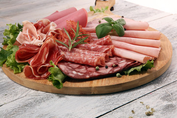 Food tray with delicious salami, pieces of sliced ham, sausage and salad. Meat platter with...