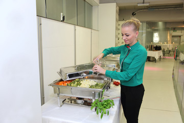 Katering, kelnerka przyprawia gotowane warzywa.