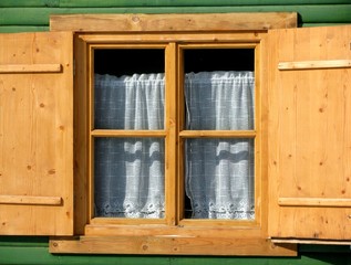 An closed window with brown natural wooden frame and open shutters