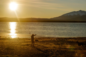 Fototapeta premium Girl and dog enjoying sunset at the beach of Puerto Natales, Patagonia, Chile