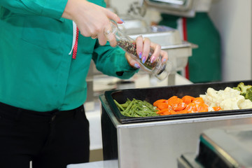 Kelnerka posypuje pieprzem gotowane warzywa na kateringu. - obrazy, fototapety, plakaty