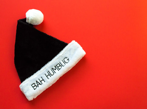 black and white fur pompom hat with the words Bah Humbug on the brim isolated on a red background with copy space
