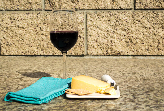red wine, cheddar cheese, crackers and knife on a small plate next to a green linen napkin on an outdoor marble counter with copy space - Powered by Adobe