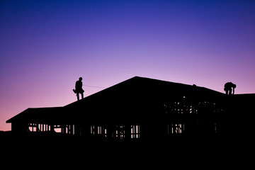 Silhouette of builders working on new construction home during sunset