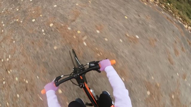 Pov view. One caucasian children rides bike road in autumn park. Little girl riding black orange mtb cycle in forest. Kid goes do bicycle sports. Biker motion ride with backpack and helmet.