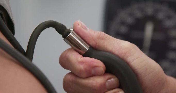 Close up of doctors hand pumping air with ball to measure patients blood pressure. Tight shot of medical practitioner measuring blood pressure with gauge