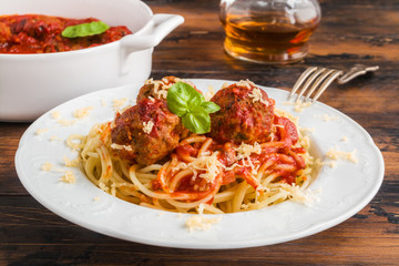 Pasta and meatballs with tomato sauce, white casserole and plate on wooden rustic table
