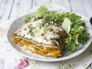 Slice of Pumpkin and Spinach Lasagne with blue cheese and salad on a White Wooden Table. Selective focus, copy space, closeup