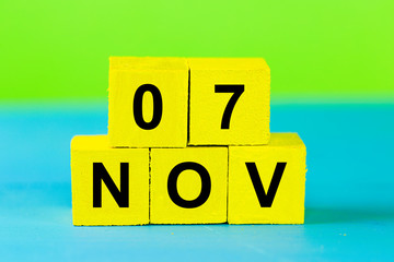 NOV 7, yellow cube calendar on blue wooden surface with copy space