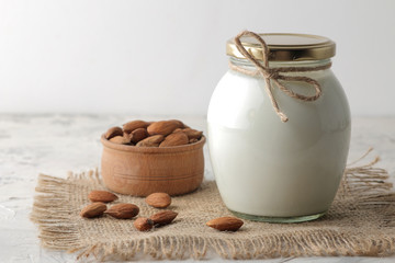 Fresh almond milk in a glass bottle and almond nuts on a light background