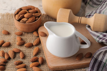 Fresh almond milk in a milk jug and almond nuts on a light background
