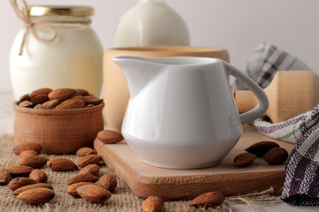 Fresh almond milk in a milk jug and almond nuts on a light background