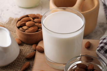 Fresh almond milk in a glass and almond nuts on a light background