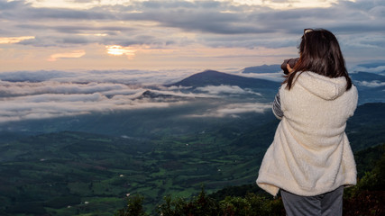 Naklejka premium Woman tourist are using a DSLR camera photographing nature landscape the sun fog mountain in the winter during sunrise on high viewpoint at Phu Ruea National Park, Loei province, Thailand