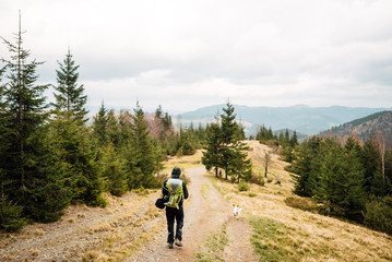 Man with a backpack walking along the road. There are mountains on the horizon. The sky is blue and cloudy.