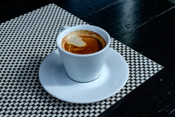 Close up beautiful white coffee cup with foam of morning, breakfast espresso with latte art on the black vintage wooden table Dark black and white space background Trendy toning Hot Latte Art coffee