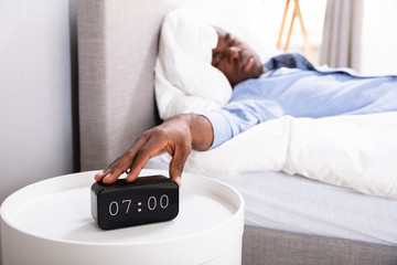 Man Sleeping On Bed Turning Off Clock