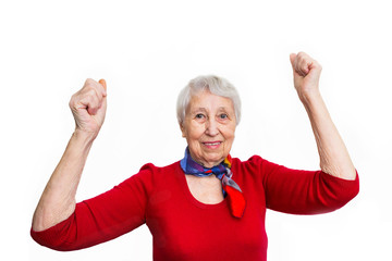 portrait of a mature woman doing a winner gesture. Old smiling woman with surprised expression on her face on studio background. Human emotions concept. Positive emotional old lady standing indoor