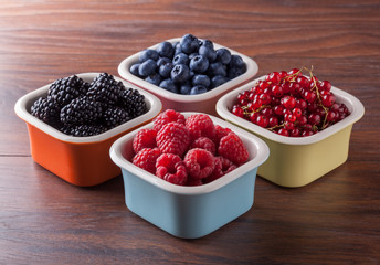 Berries fresh arrangement raspberries blackberries blueberries and red currant in colored ceramic jars front view on brown table in studio