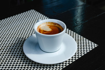 Close up beautiful white coffee cup with foam of morning, breakfast espresso with latte art on the black vintage wooden table Dark black and white space background Trendy toning Hot Latte Art coffee