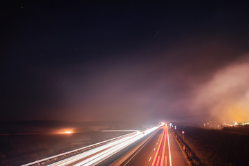 Fototapeta na wymiar German motorway view with night stars sky and fog that glow from cars light trails showing the speed and motion from the traffic. Braunschweig, Germany