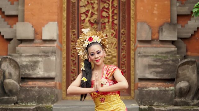Beautiful balinese woman with traditional dress smiling at the camera and showing welcome gesture in a hinduism temple. Shot in 4k resolution