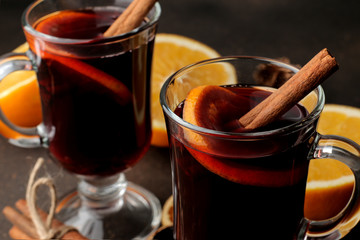 Hot mulled wine with cinnamon and orange in glass cups close-up on a dark background. Christmas....