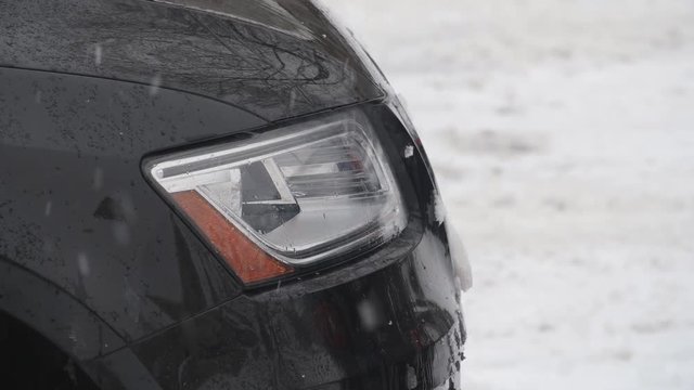 Headlight of black suv vehicle with snow falling. Winter driving in Canada.