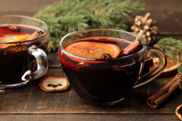 Hot mulled wine with cinnamon and orange in glass cups and Christmas decorations on a dark...