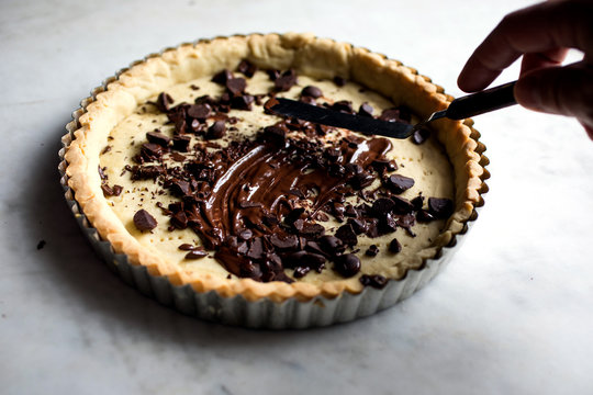 Man's hand spreading chocolate on tangerine tart