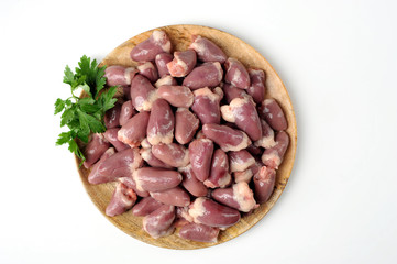  Raw chicken hearts on a round wooden tray. The product is decorated with parsley. White background. Close-up. View from above.