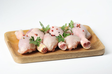 Raw chicken drumstick on a light wooden tray. Chicken legs are decorated with parsley and spices. White background. Close-up.