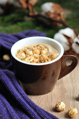 A cup of coffee and caramel popcorn. Next to the cup there is a warm scarf, cotton flowers and a fir branch. Light background. Close-up. Vertical frame orientation.