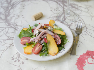 Salad with persimmon, smoked chicken, cherry tomatoes, Camembert cheese and blue cheese sauce. Festive dish . Christmas dinner. Selective focus, closeup, copy space