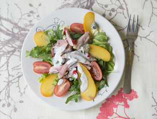 Salad with persimmon, smoked chicken, cherry tomatoes, Camembert cheese and blue cheese sauce. Festive dish . Christmas dinner. Selective focus, closeup, copy space, top view
