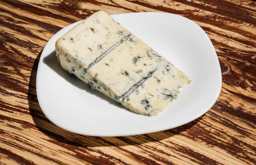 Soft and creamy. Blue cheese food. Piece of cheese on plate. Roquefort cheese. Gorgonzola cheese. Italian or danish cuisine on wooden table. Dairy food