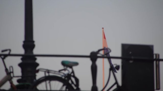 Passing under a bridge with a bicycle locked to the railing in silohuette while watching the Dutch flag of the Netherlands wave in the breeze beyond