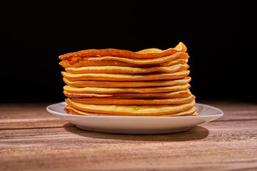 Stack of pancakes on a plate with a black background at the back