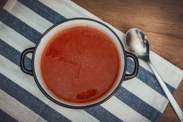 Fresh tomato soup with greens in a bowl on striped tablecloth
