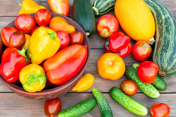 Vegetables: tomatoes, cucumbers, paprika, pepper, zucchini in a clay bowl and on a wooden table. Ingredients for the preparation of summer vegetable salad