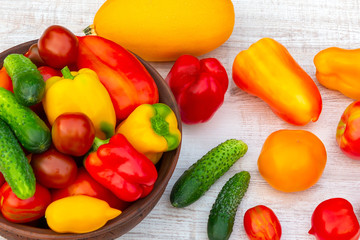Vegetables: tomatoes, cucumbers, paprika, pepper, zucchini in a clay bowl and on a white wooden...
