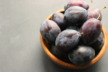 Close-up of many ripe plums in a wooden bowl on a black wooden background. Juicy fruits, healthy food, vitamins, veganism, organic products