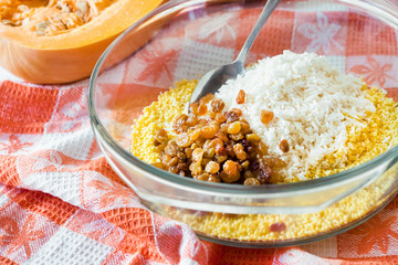 Raw washed millet, rice and raisins in a glass pan in the process of preparing milk pumpkin porridge